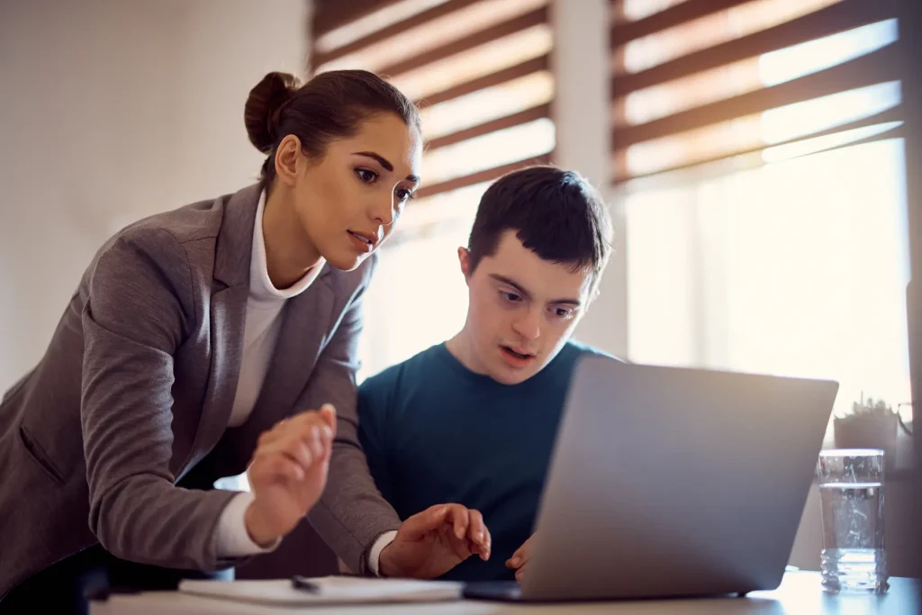 female support worker helping disabled boy on computer