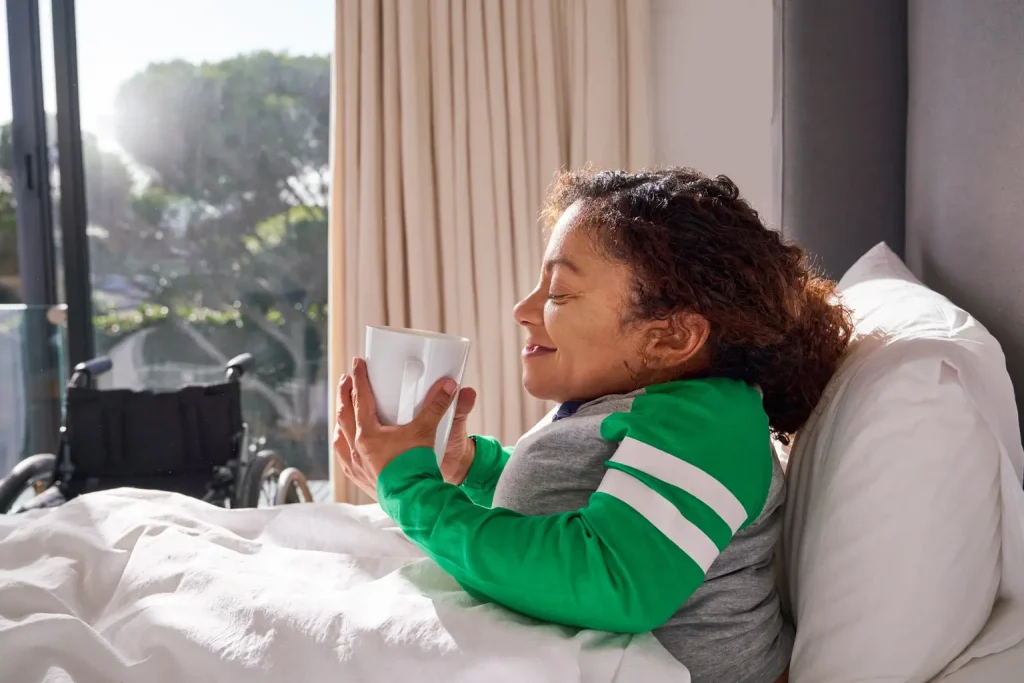 Disabled woman lying in bed enjoying a warm drink