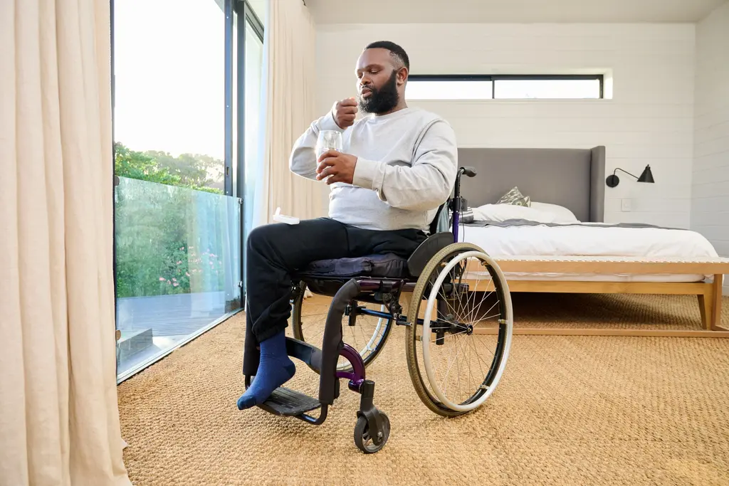 Man in wheelchair in bedroom drinking a glass of water